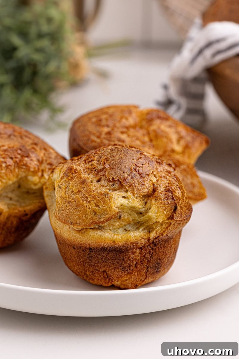 Three golden popovers arranged on a simple white plate, ready to be enjoyed.