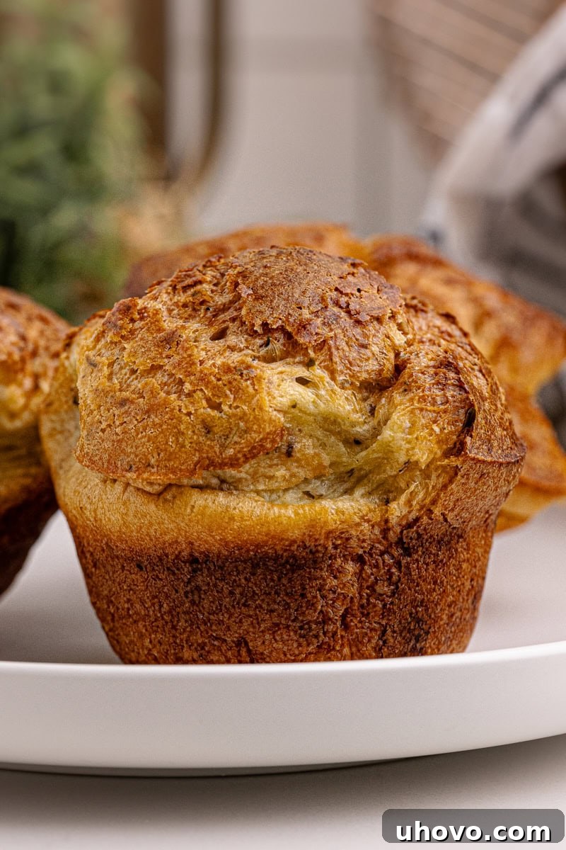 Close-up of a single golden, perfectly risen popover on a white plate, showcasing its crispy exterior and hollow interior.