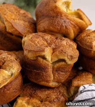 Golden, fluffy popovers piled high in a towel-lined wooden bowl.