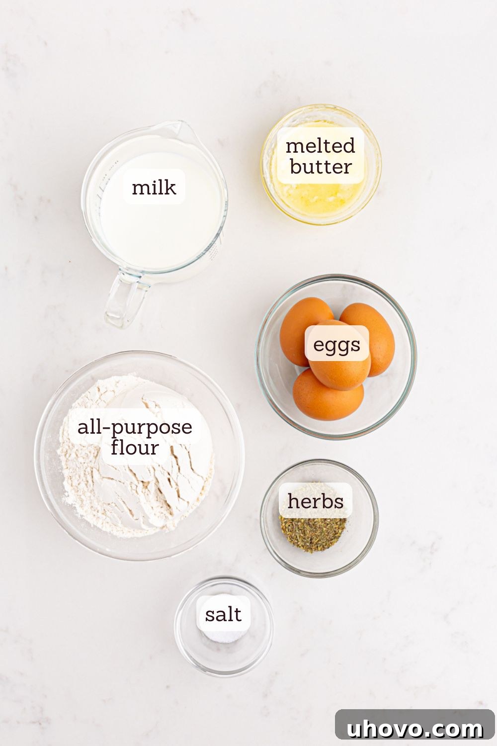 Overhead view of fresh popover ingredients including eggs, milk, flour, and butter, neatly arranged on a wooden surface.