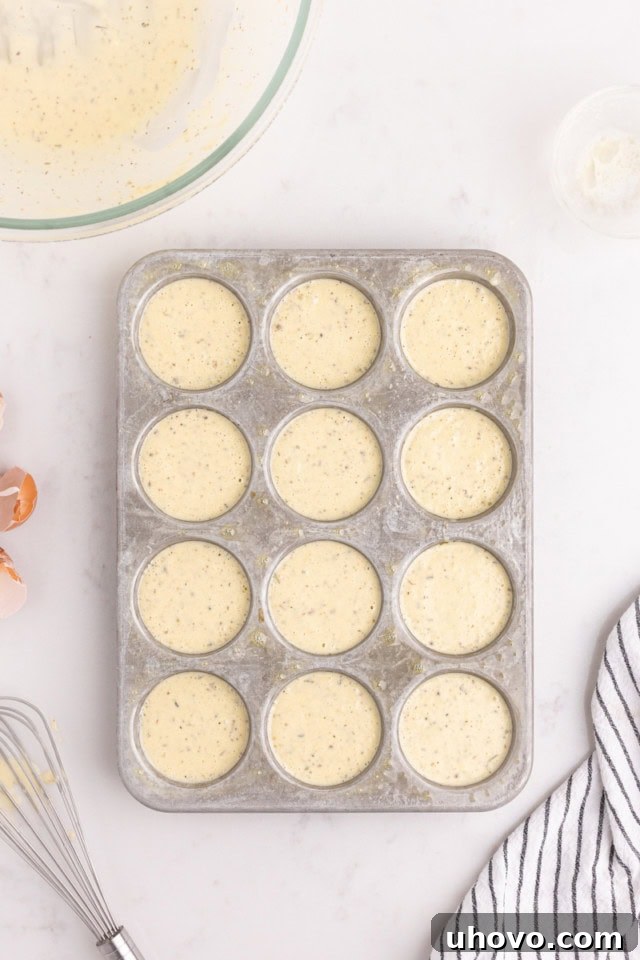 Overhead view of popover batter precisely divided into the greased cups of a standard muffin pan, ready to bake.