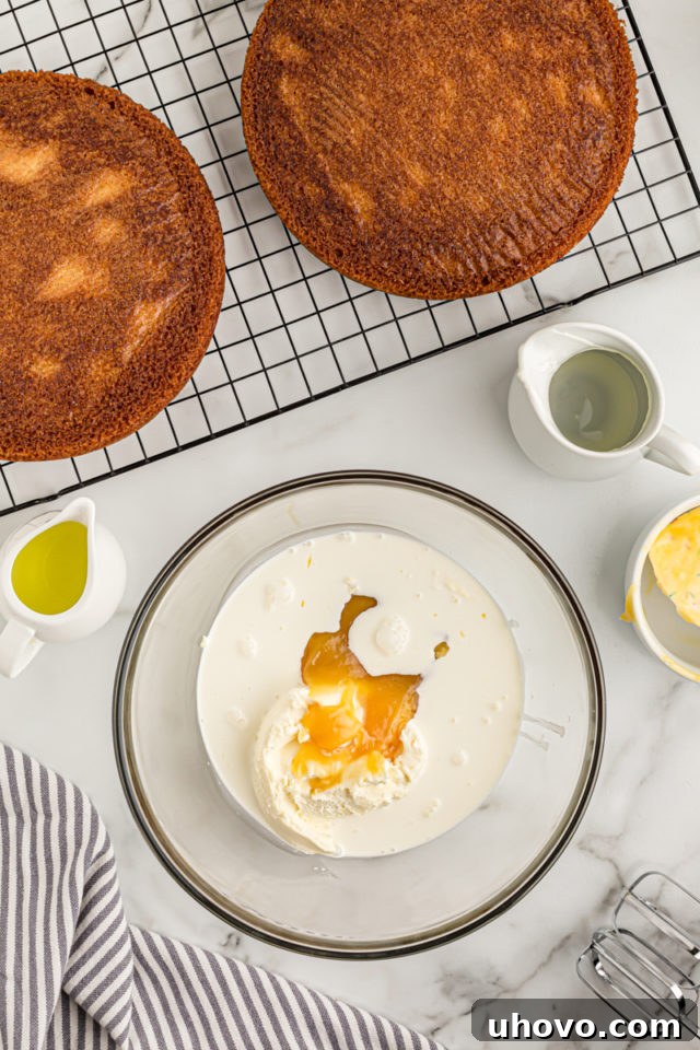 Overhead view of the mascarpone frosting ingredients – mascarpone cheese, heavy cream, and lemon curd – in a clear glass mixing bowl, ready to be whipped.