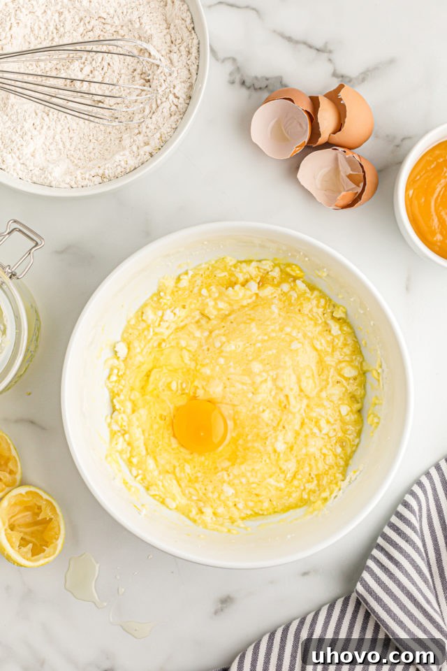 Overhead view of a single egg being added to the butter and sugar mixture in a mixing bowl, part of the lemon cream cake batter preparation.