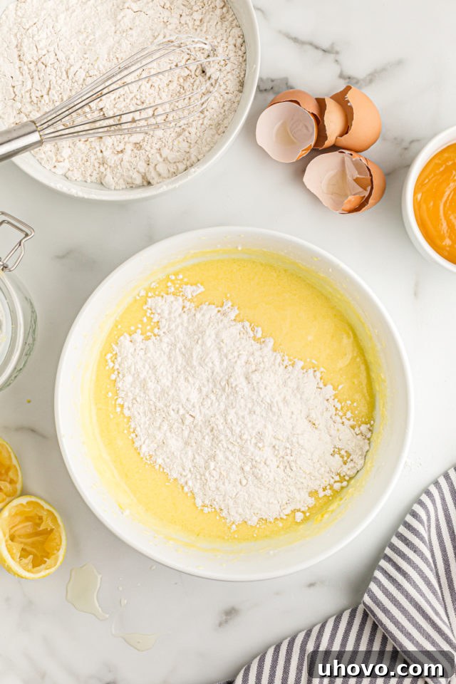 Overhead view of dry ingredients being carefully poured into the bowl of wet cake batter, ready for final mixing.