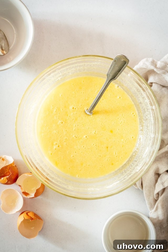 Overhead view of the smooth, pale yellow lemon curd mixture in a mixing bowl with a spoon, perfectly blended and ready for baking.
