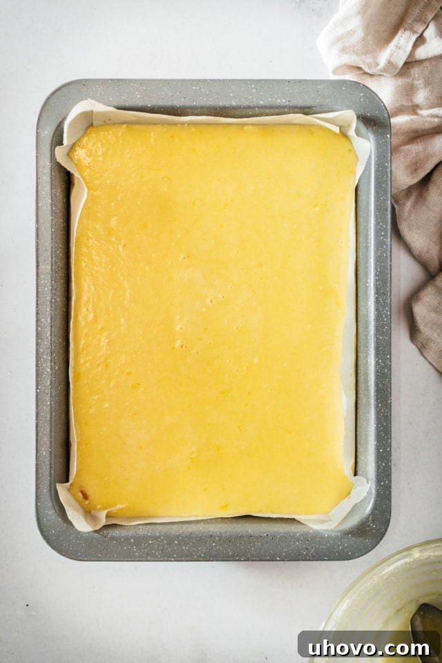 Overhead view of the raw lemon filling poured over the par-baked crust in the baking pan, ready to be placed back into the oven.