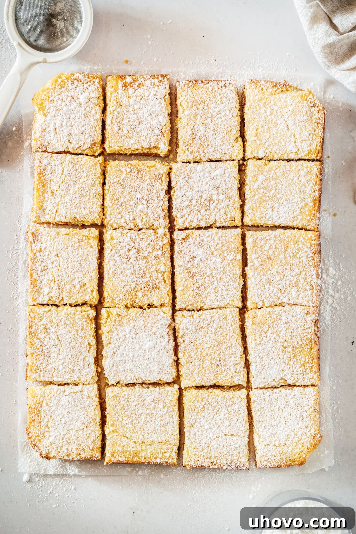 Overhead view of the entire pan of baked lemon bars, still intact on the parchment paper, showcasing their golden edges and smooth, set filling.