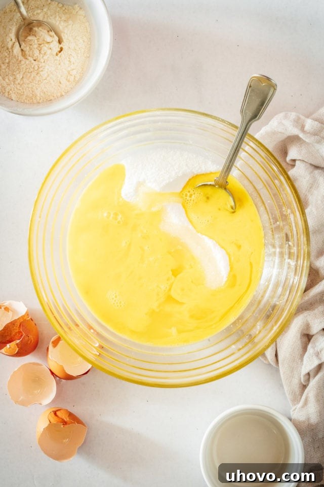 Overhead view of granulated sugar being stirred into a bowl with eggs and lemon juice, creating the initial liquid base for the filling.