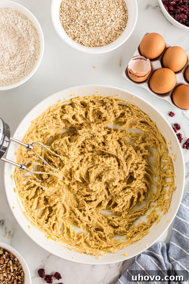 A close-up, overhead view of perfectly mixed wet ingredients for oatmeal cranberry cookies, showcasing a smooth, creamy, and uniform golden batter in a white mixing bowl, ready for dry additions.