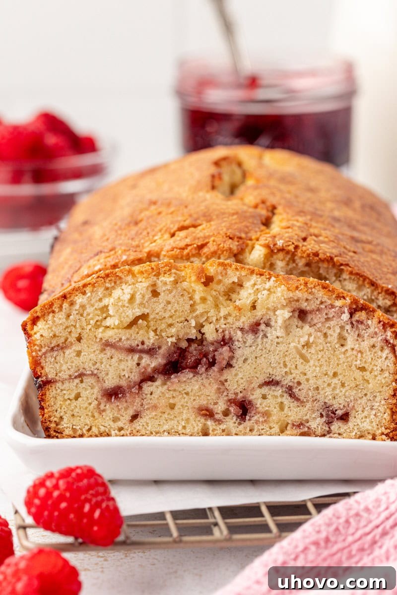 A partially sliced berry swirl pound cake presented on a white serving tray, showcasing its beautiful interior swirl.