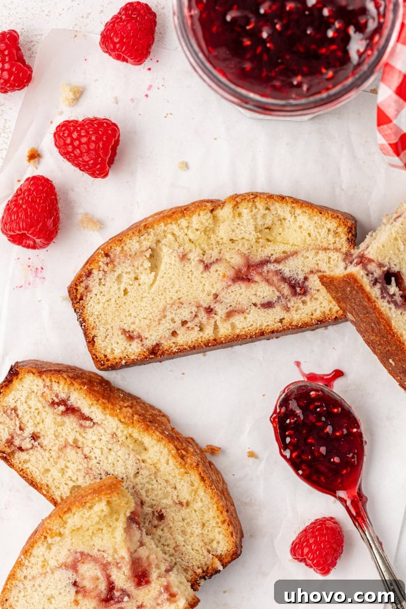 A few slices of berry swirl pound cake arranged on parchment paper, accompanied by fresh raspberries and a spoonful of raspberry preserves, highlighting its rustic elegance.