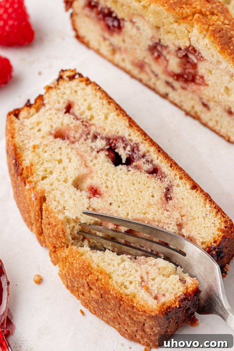 A fork gently cutting into a slice of berry swirl pound cake, revealing its moist texture and vibrant fruit swirl.