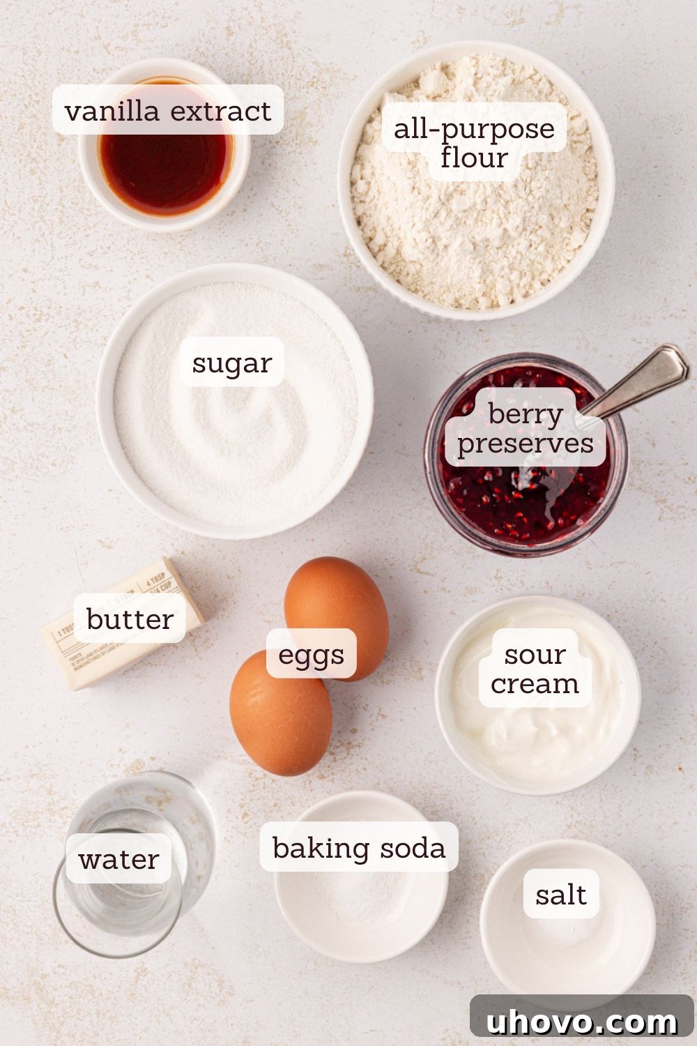 Overhead view of various ingredients for berry swirl pound cake laid out on a surface, including flour, sugar, butter, eggs, sour cream, and berry preserves.