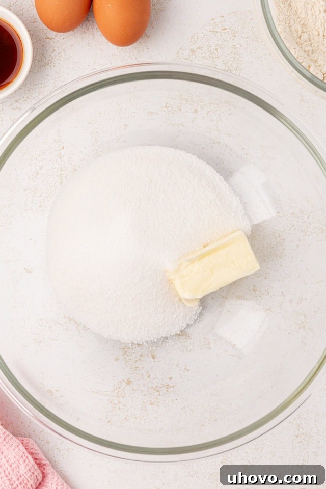 Overhead view of softened butter and granulated sugar in a glass mixing bowl, being creamed together.