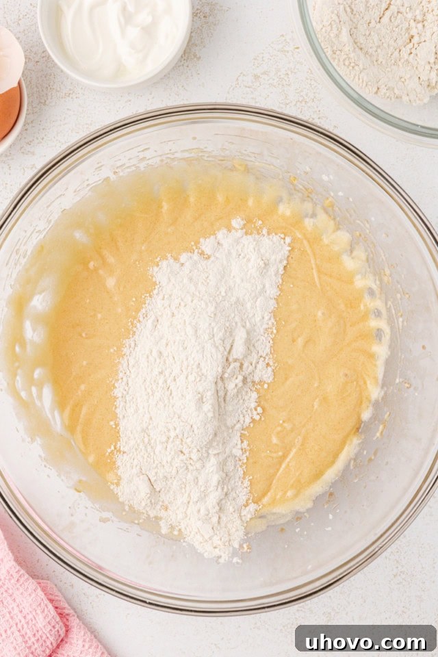 Overhead view of dry ingredients being gradually added to the wet ingredients for berry swirl pound cake batter.