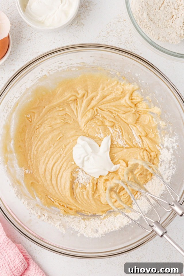 Overhead view of sour cream being added to berry swirl pound cake batter, alternating with dry ingredients.