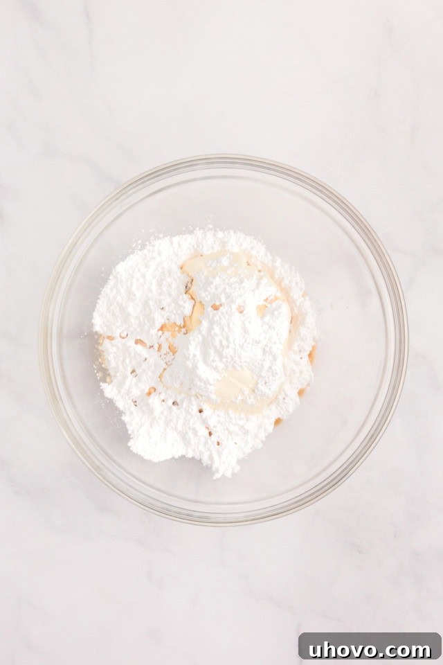 overhead view of confectioners' sugar, ricotta, and vanilla in a glass mixing bowl