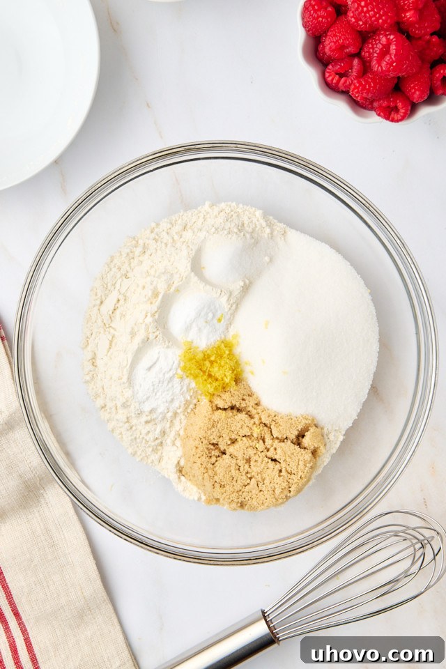 An overhead shot of dry ingredients, including flour, sugar, and baking powder, mixed together in a large glass mixing bowl.