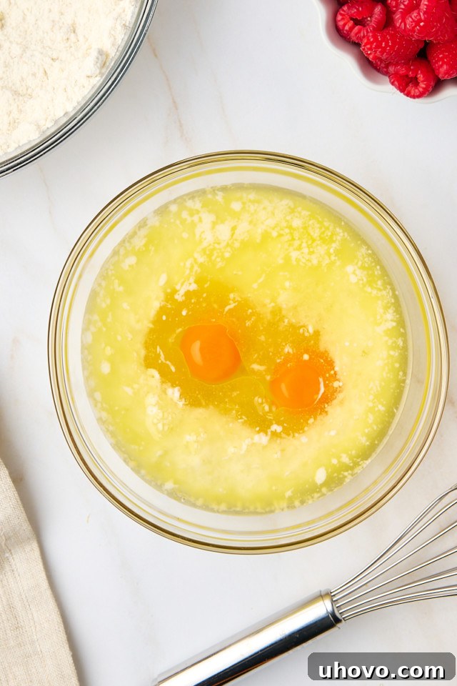 An overhead shot of wet ingredients, including melted butter, milk, and eggs, being whisked together in a separate mixing bowl.