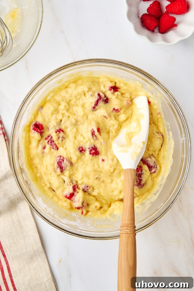 An overhead shot of lemon raspberry muffin batter in a mixing bowl, showing it's just mixed with a few streaks of flour remaining, indicating no over-mixing.