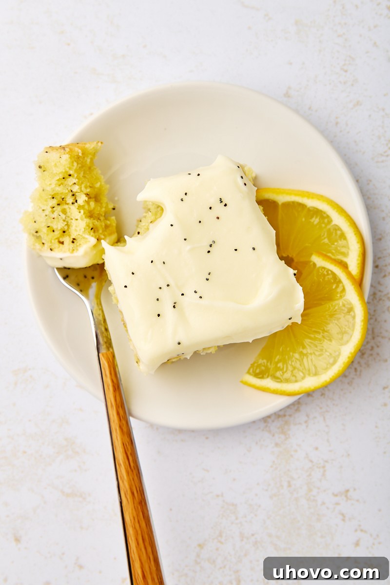 overhead view of a slice of lemon poppy seed cake with a bite on a fork, served on a white plate with two lemon slices