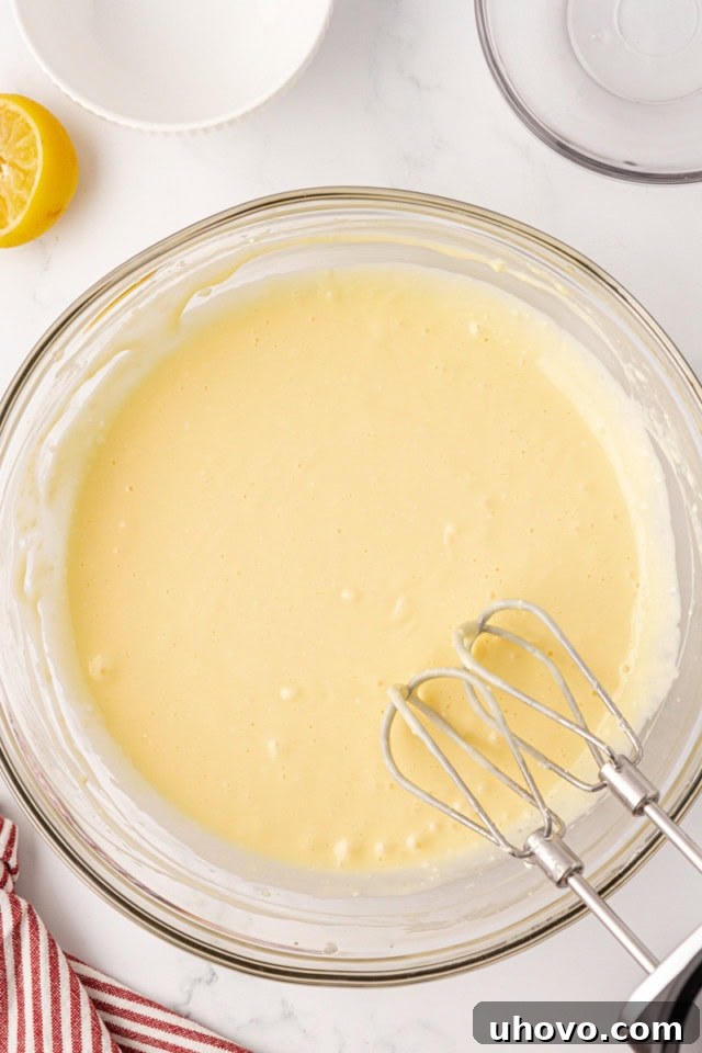 An overhead shot of the cheesecake batter in a glass mixing bowl, showing its perfectly smooth and creamy texture after being beaten, ready for the crust.