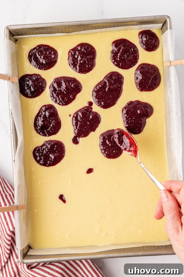 An overhead view of the cherry topping being carefully spooned in small dollops onto the smooth cheesecake batter, preparing for the swirling step.