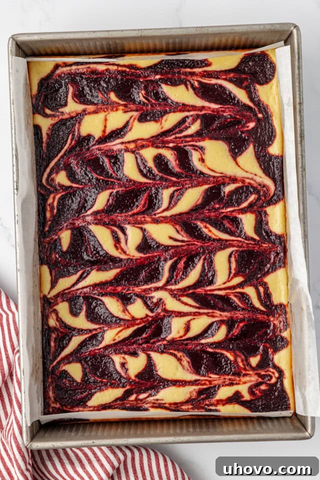An overhead view of the freshly baked cherry cheesecake bars in a 9x13 inch baking pan, showcasing the set cheesecake and vibrant cherry swirls, cooling on a wire rack.