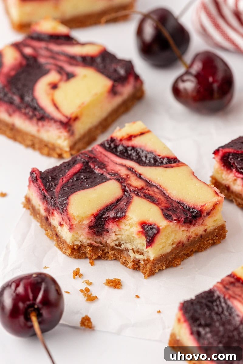 A close-up of a cherry cheesecake bar with a bite taken out, resting next to more uncut bars and fresh cherries in the background, inviting viewers to indulge.