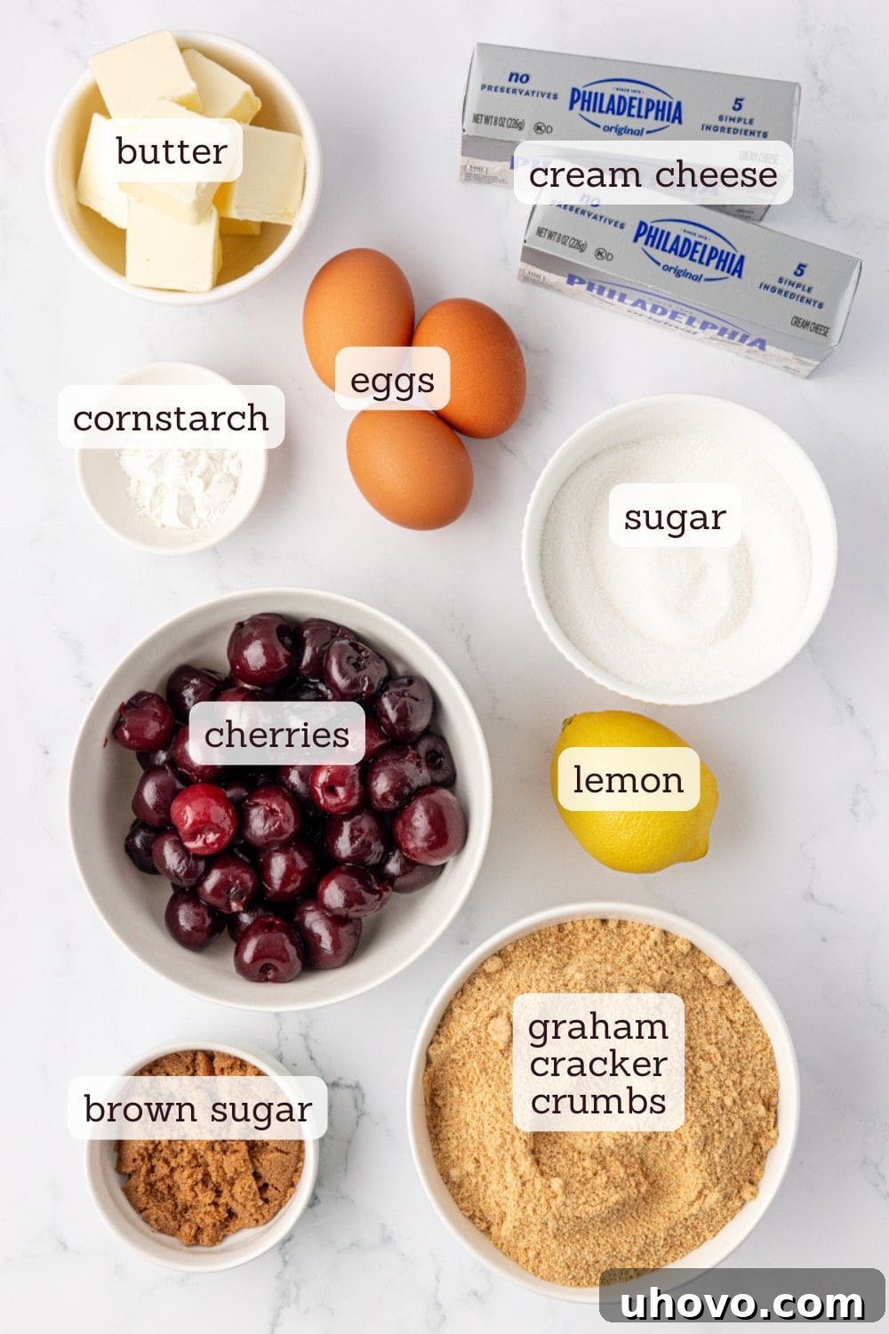 An overhead shot showcasing all the essential ingredients laid out for making delicious cherry cheesecake bars, including fresh cherries, blocks of cream cheese, graham crackers, butter, sugar, and lemons.