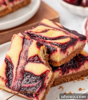 A cherry cheesecake bar leaned against a stack of two more bars; fresh cherries and more bars partially visible in the background