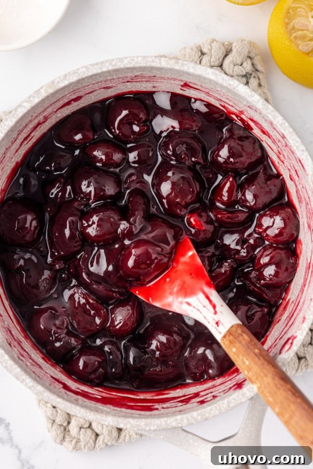 An overhead view of the cherry topping in a saucepan, thickened to a glossy, rich consistency after being cooked with cornstarch and lemon, showcasing its readiness for the next step.