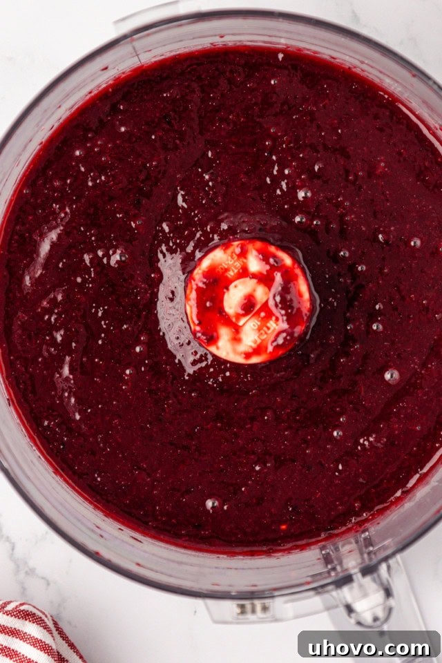 An overhead view of the blended cherry topping in a bowl, now a smooth, vibrant purée, ready to be swirled into the cheesecake filling.