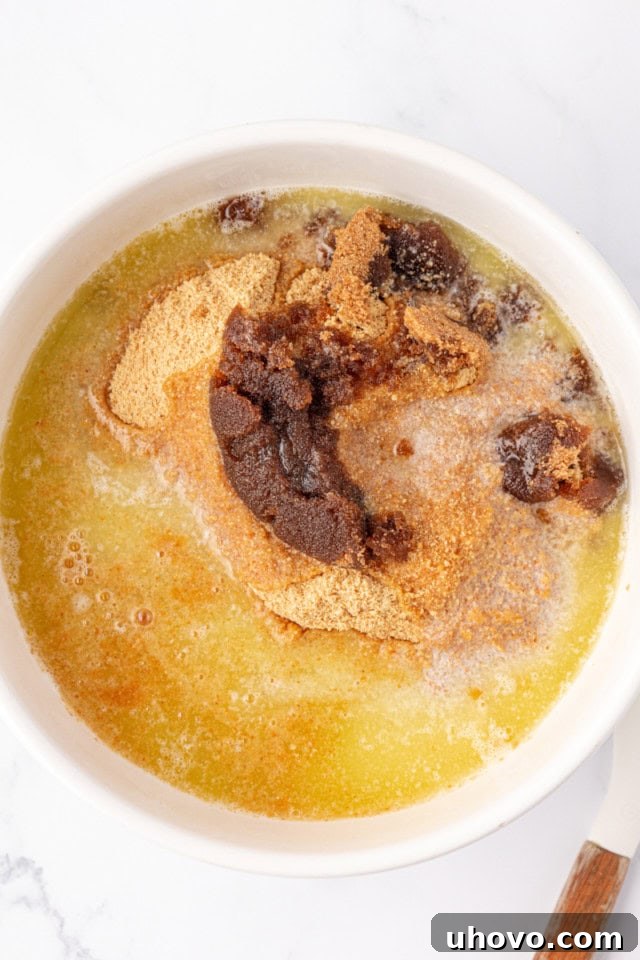 An overhead view inside a mixing bowl, showing graham cracker crumbs, rich brown sugar, and melted butter being combined, the foundational ingredients for the crust.