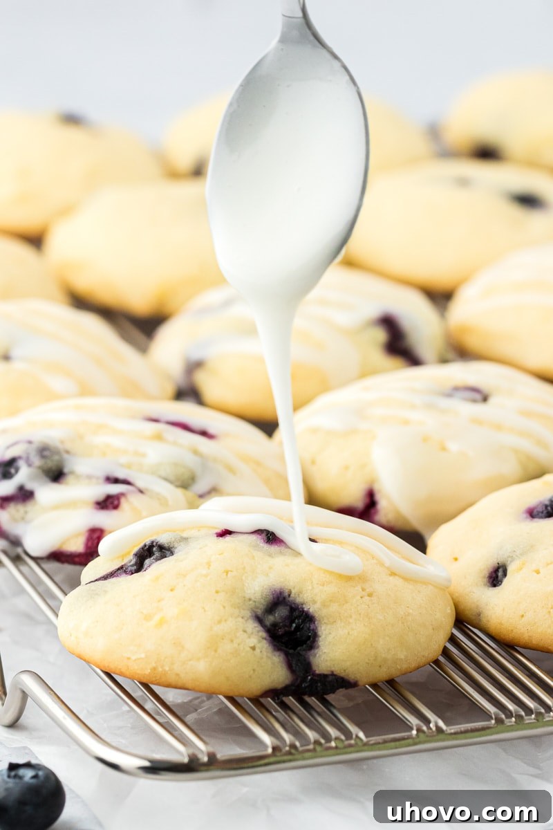 lemon glaze being drizzled over lemon blueberry cookies on a wire rack