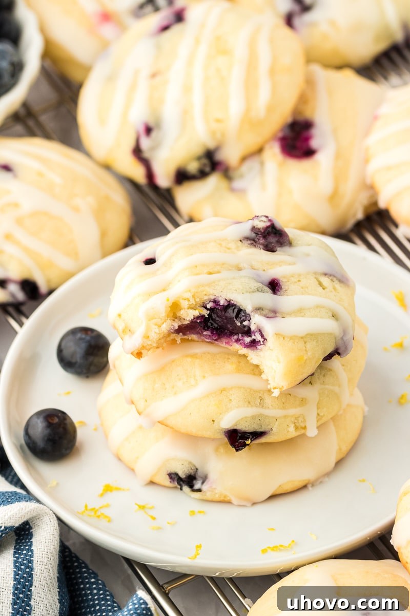 a stack of three lemon blueberry cookies on a white plate with more cookies surrounding