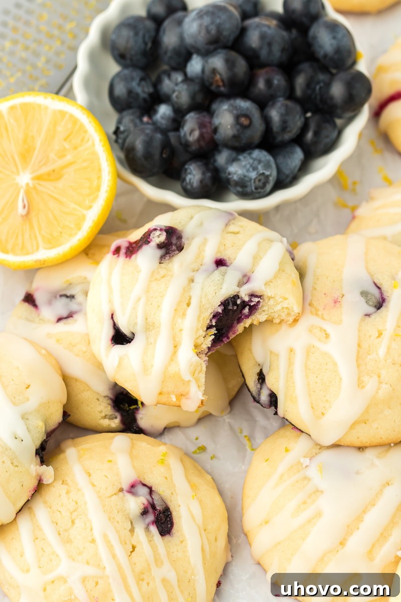 a lemon blueberry cookie with a bite missing on top of more cookies with a bowl of blueberries in the background