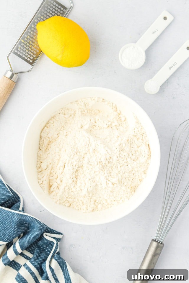 overhead view of flour, baking powder, salt, and lemon zest in a white mixing bowl