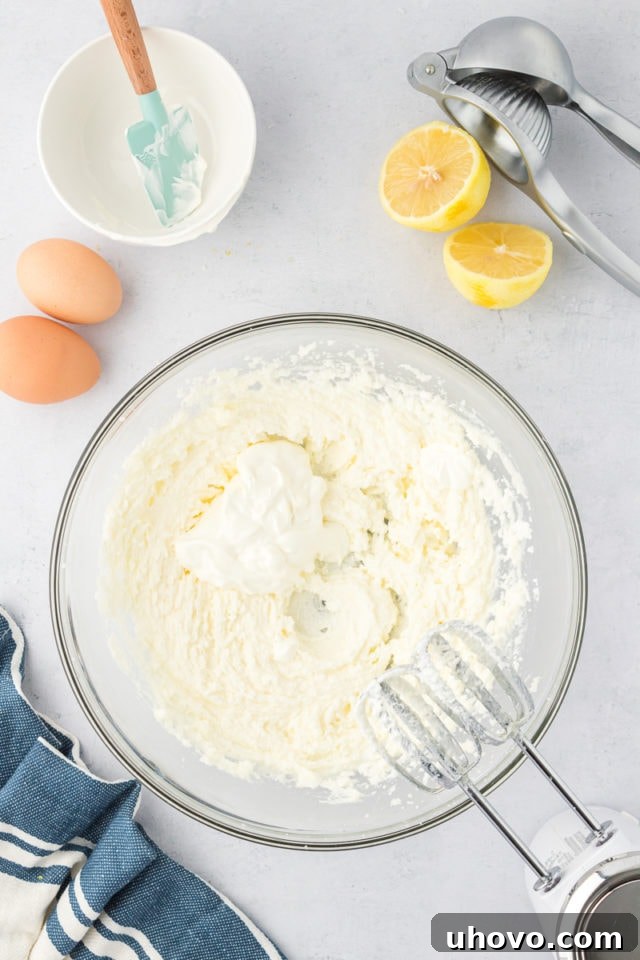 overhead view of sour cream added to creamed butter and sugar in a glass mixing bowl