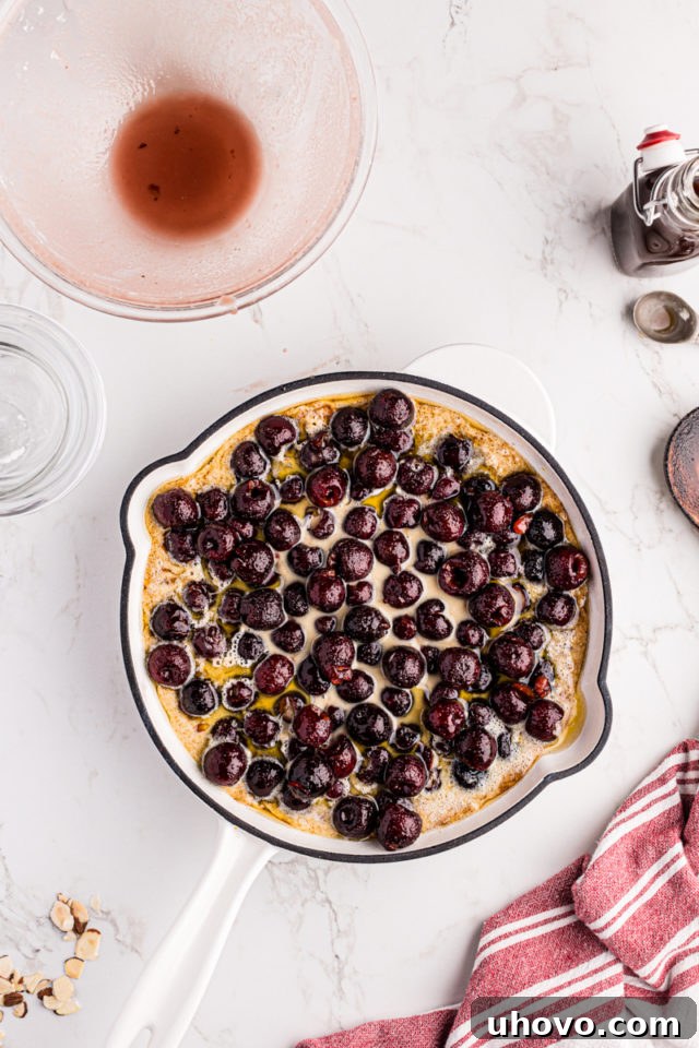 Overhead view of the cherry mixture being spooned carefully and evenly over the cobbler batter in the skillet, creating the fruit layer.
