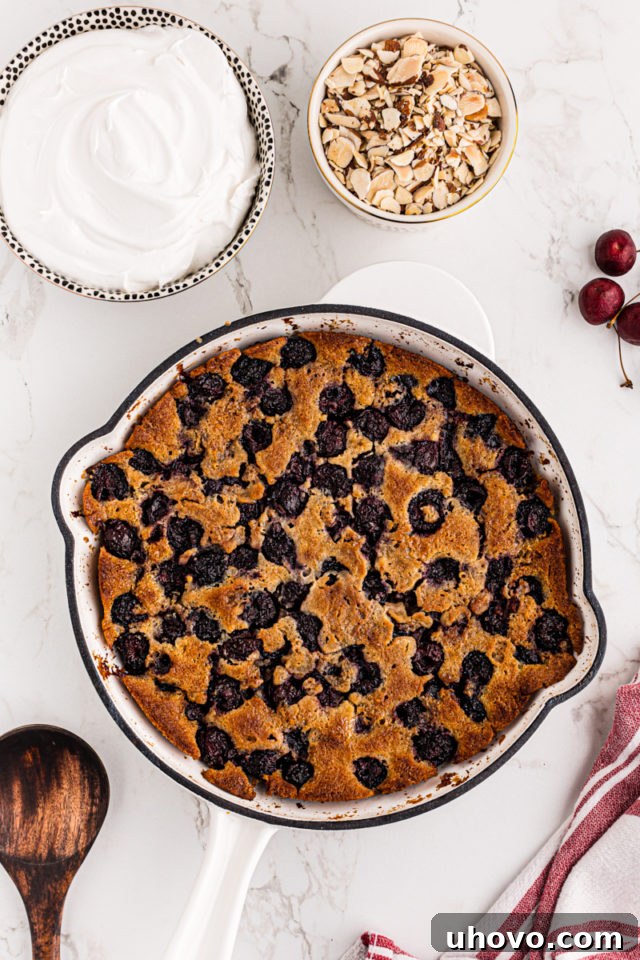 Overhead view of the assembled brown butter cherry cobbler in the skillet, golden brown and bubbly, surrounded by bowls of whipped cream and almonds, ready for serving.
