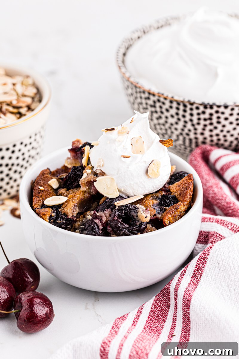 A white bowl showcasing brown butter cherry cobbler topped with a generous dollop of homemade whipped cream, ready for a delightful indulgence.