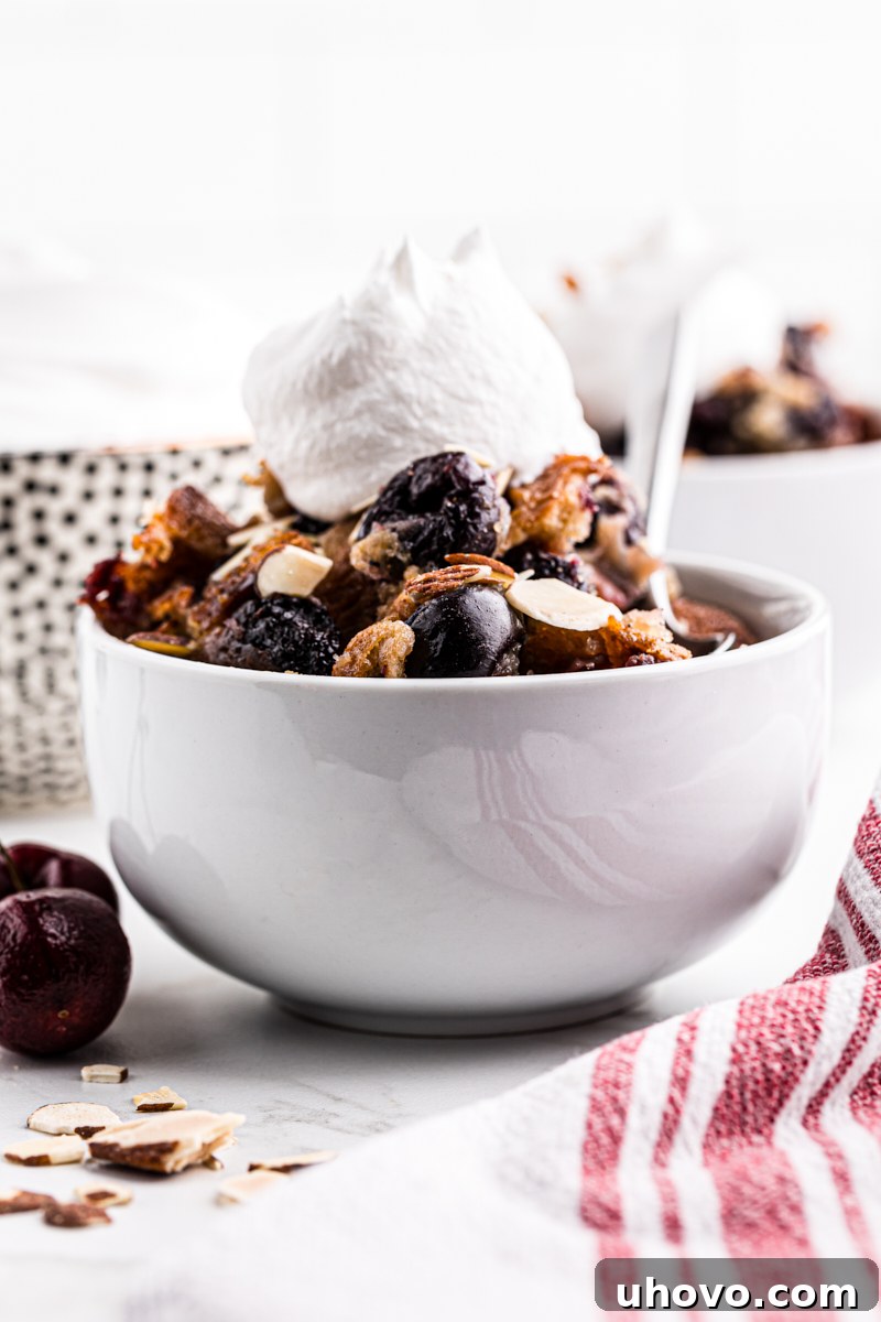 A close-up of a bowl filled with brown butter cherry cobbler, adorned with a delicate dollop of whipped cream, inviting a taste.