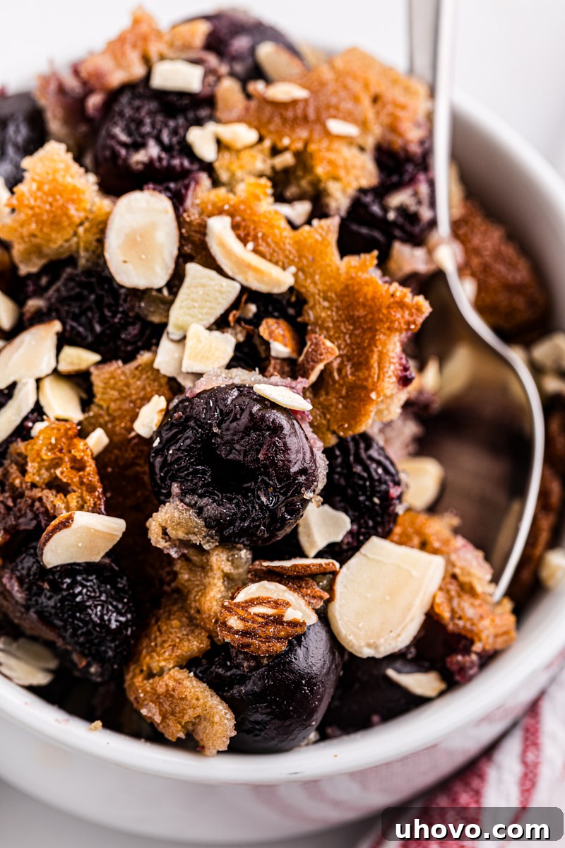 Overhead view of a bowl of brown butter cherry cobbler with a spoon resting in it, showcasing the inviting texture of the fruit and crust.