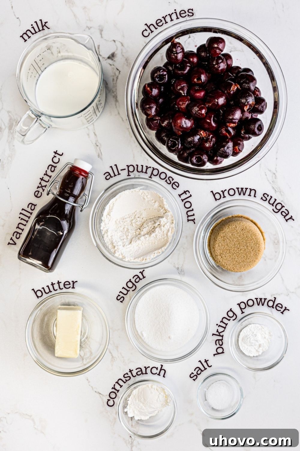 All ingredients for brown butter cherry cobbler neatly arranged on a white surface, including fresh cherries, butter, flour, sugar, and milk, ready for preparation.