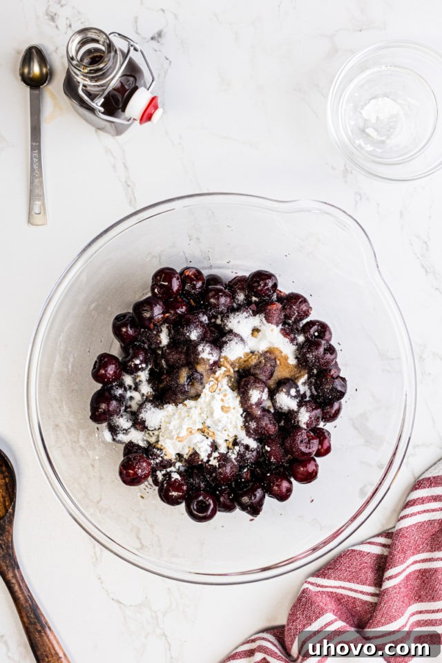 Overhead view of fresh cherries, granulated sugar, cornstarch, and vanilla extract combined in a mixing bowl for the cherry filling.