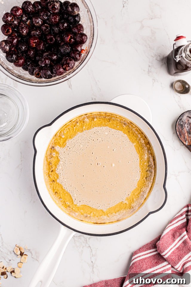 Overhead view of the cobbler batter being poured evenly over the warm brown butter in the skillet, forming the base layer.