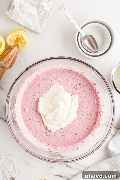 Overhead view of whipped cream being gently folded into the berry cheesecake filling