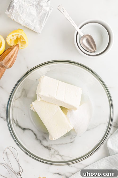Overhead view of cream cheese, remaining sugar, and lemon juice in a mixing bowl