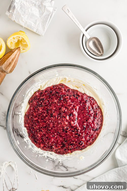 Overhead view of the berry puree being added to the beaten cream cheese mixture in a bowl